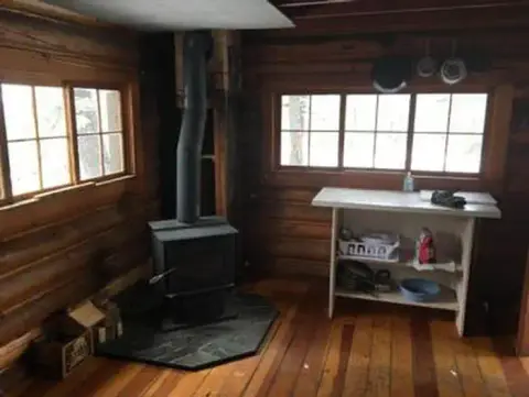 An interior view of a rustic log cabin with a wood stove and a small table.