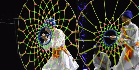 Performers dance while holding large webbed wheel props.