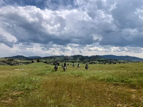 A group of people ride horses across a grassy field under a cloudy sky.