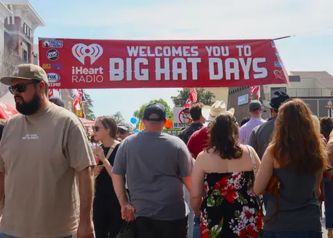 A large crowd of people walking underneath a banner welcoming visitors to an outdoor festival.