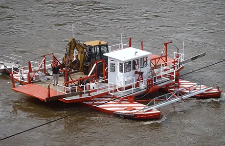 A work barge carrying an excavator on a river.
