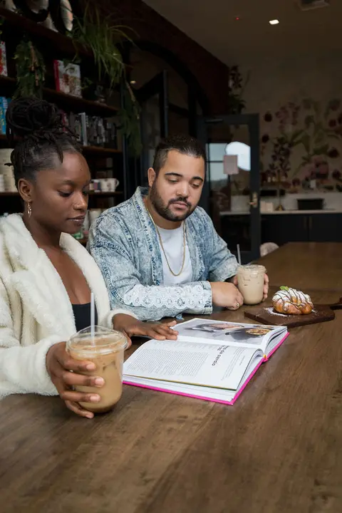 A man and a woman look at a book in a cafe.