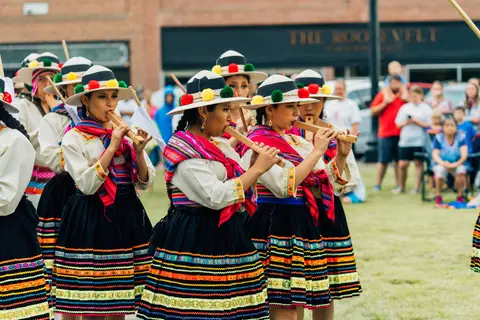 A group of women in traditional clothing play flutes during an outdoor performance.