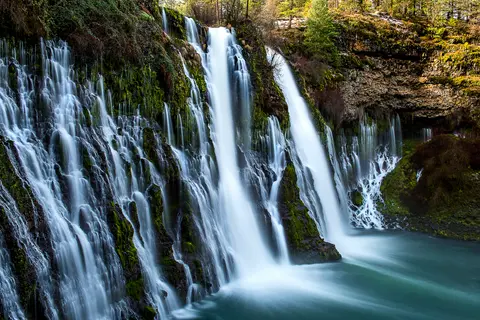 A long exposure photograph shows multiple streams of water cascading over a mossy cliff into a pool.
