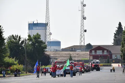 A group of people holding flags and a banner walks down a street in a parade.