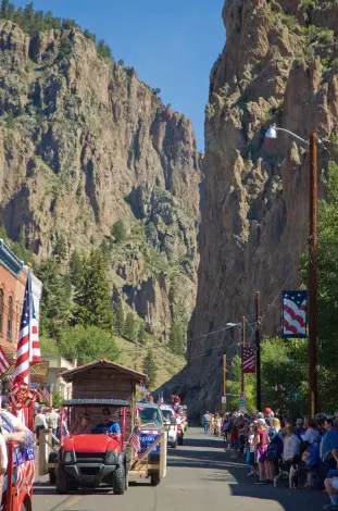 A parade on a street framed by large rocky cliffs and a crowd of people watching.