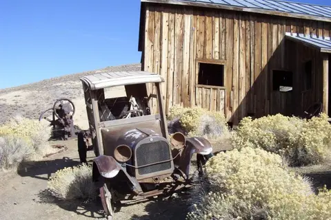 An old rusted car parked outside a rustic wooden building.