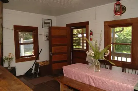 Interior view of a rustic room with a wooden table, chairs, and red lantern.