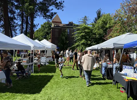 A crowd of people browsing tents at an outdoor market on a sunny day.