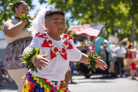 A young boy dances in traditional attire with floral leis and a feather headpiece.