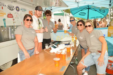 A group of people standing behind a counter with drinks at an outdoor event.