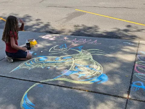 A young girl draws with chalk on a sidewalk.