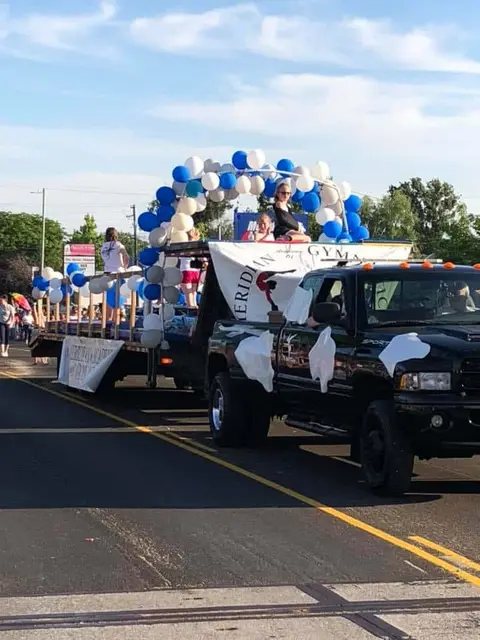 A truck pulls a parade float decorated with balloons and carrying people.