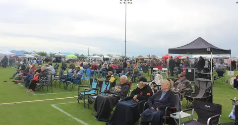 A crowd of people seated on chairs in a field watching an outdoor event.