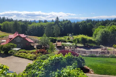 An elevated view of a farm property with a barn, round pen, and surrounding trees and mountains.