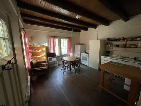 A rustic kitchen interior with exposed wooden ceiling beams and a dining table.