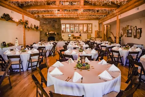 A spacious rustic lodge interior is set up with round tables for an event.