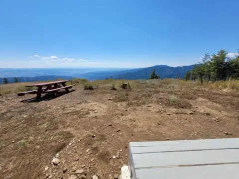A scenic overlook with a picnic table and distant mountains under a blue sky.