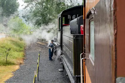 A train worker stands beside a steam train with steam rising from the tracks.
