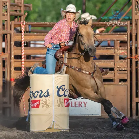 A cowgirl on a horse races around a barrel in an arena.