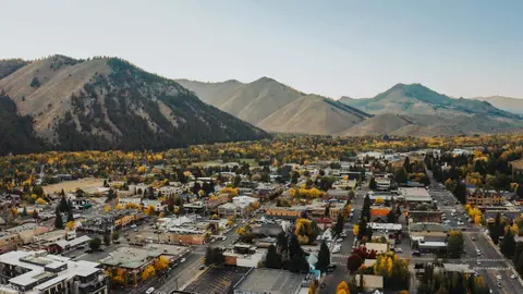 An aerial view of a town nestled beneath mountains with autumn trees.