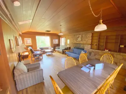 A spacious rustic room featuring a dining table in the foreground and a sitting area with a fireplace in the background.