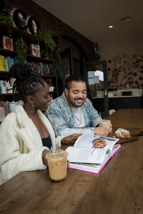 Two people sitting together at a table reading a cookbook in a cafe.