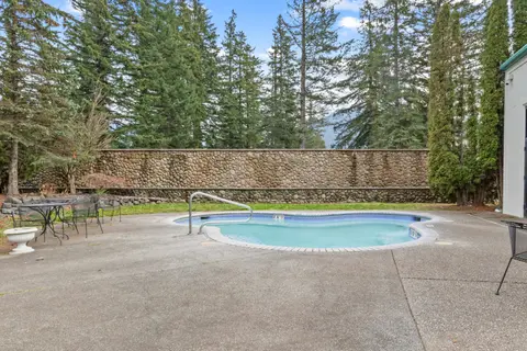 An outdoor swimming pool surrounded by a stone wall and tall evergreen trees.
