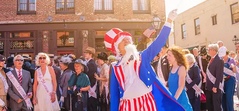 A person dressed as Uncle Sam stands before a crowd outdoors.