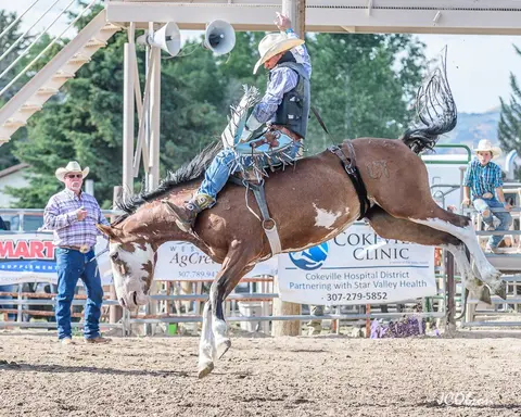 A cowboy rides a bucking horse at a rodeo.