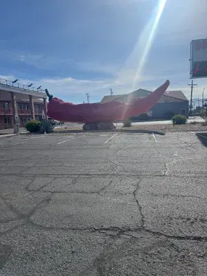 A giant red chili pepper sculpture is displayed in a parking lot.