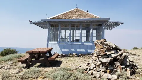 A small light-blue lookout building with a picnic table and a rock cairn outside.