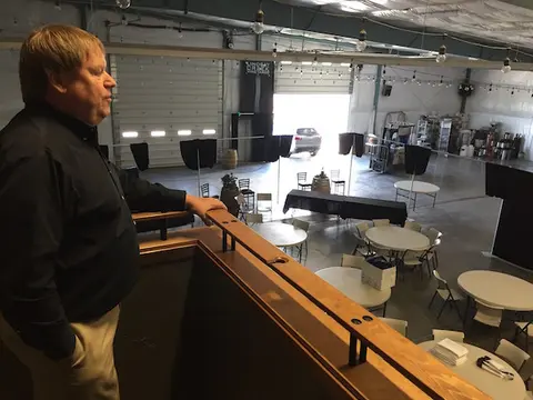 A man looks over a balcony into a large industrial-style space arranged with tables and chairs.