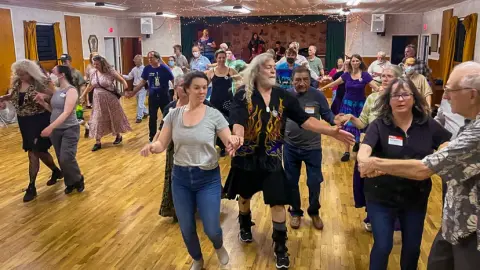 A group of people dancing in a hall with a wooden floor.