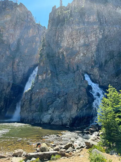 A person looks at a rocky canyon with dual waterfalls flowing into a pool.