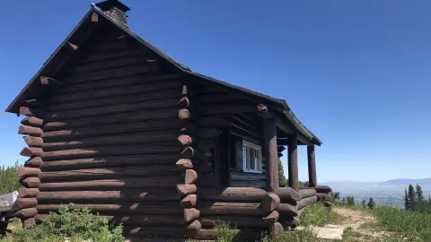 A dark brown log cabin stands under a clear blue sky.
