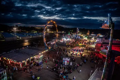 An elevated view of a crowded carnival at night with illuminated rides and tents.