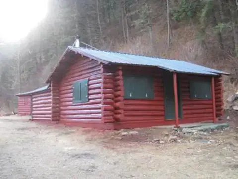 A red log cabin stands in a wooded area.