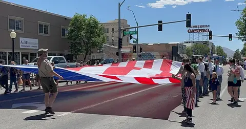 People carry a large American flag down a street during an event.