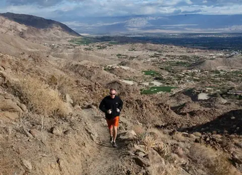 A runner on a mountain trail overlooking a valley.