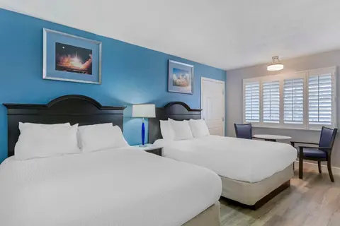 A hotel bedroom featuring two beds and a blue accent wall.