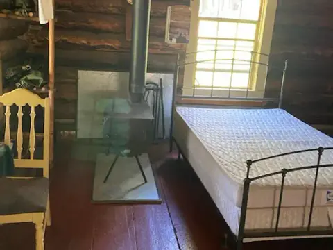 An interior view of a rustic log cabin with a bed and a wood stove.