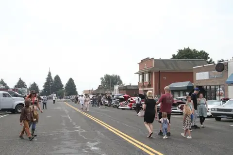 A street filled with people and classic cars during an outdoor event.