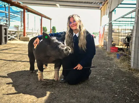 A young person kneels next to a pig in an agricultural pavilion.