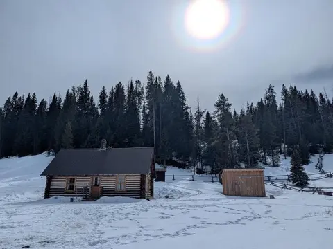 A log cabin in a snowy landscape beneath a bright sky.