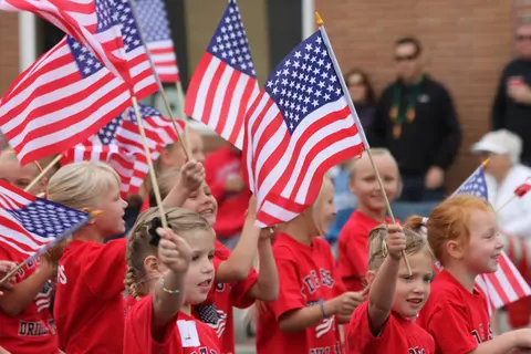 Children in red shirts hold small American flags outdoors.