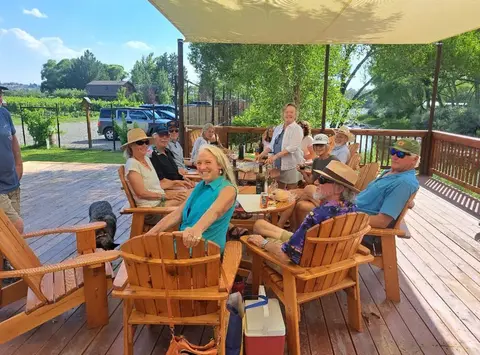 A group of people sitting at a table on a wooden deck outdoors.