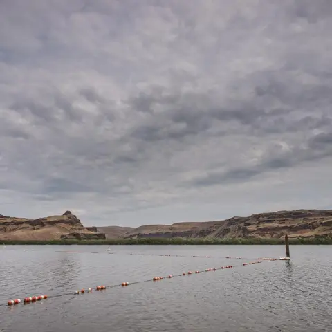 A view of a lake and surrounding hills under a cloudy sky.