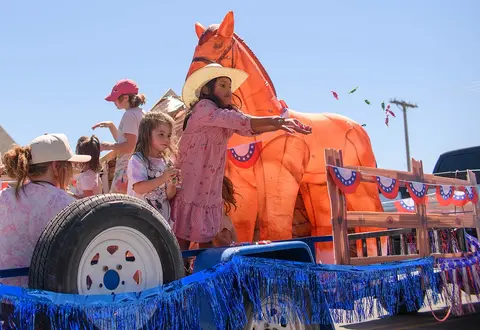 Children ride on a parade float decorated with a large inflatable horse and patriotic bunting.