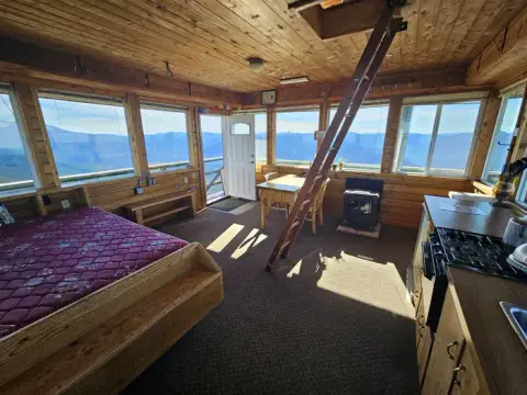 An interior view of a wooden cabin with large windows showing a mountain view.